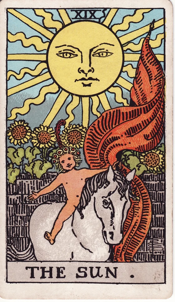 The Sun tarot card from the Rider–Waite–Smith deck: a smiling child riding a white horse holding a red banner, sunflowers over a wall, a large radiant sun above.